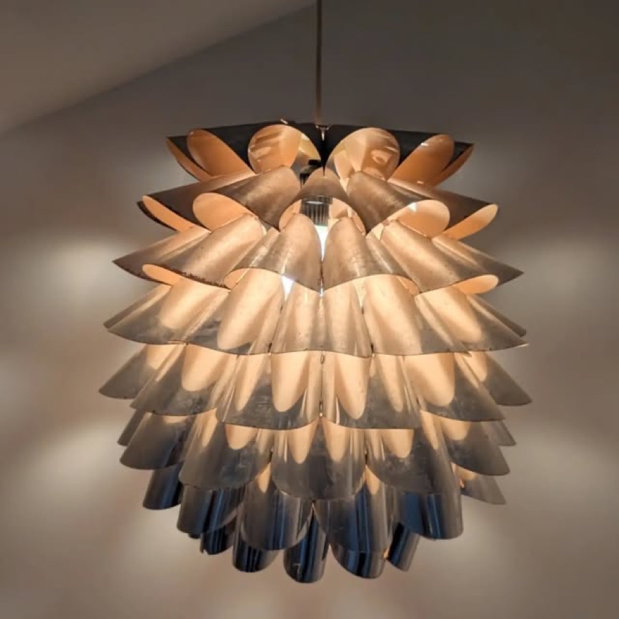 A pendant lamp made of overlapping copper petals, lit from inside so the undersides glow pale and warm.